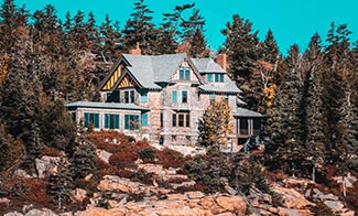gray house surrounded-by-pine trees on rocky coast