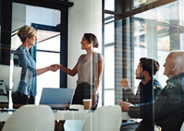 two women shaking hand in glass conference room