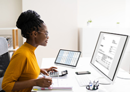 woman at desk with large monitor and calculator