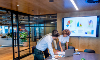 3-people-standing-around-laptop-in-conference-room