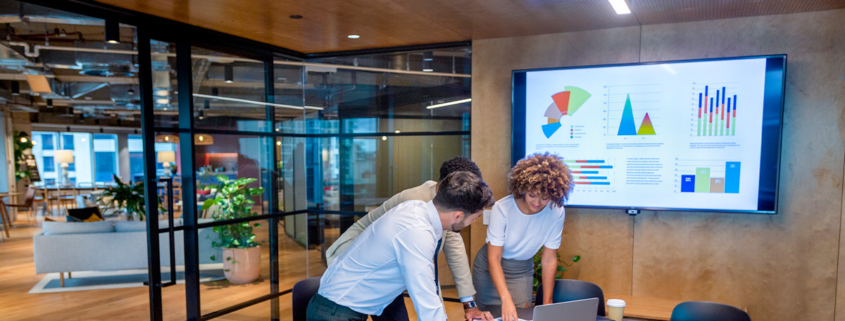 3-people-standing-around-laptop-in-conference-room